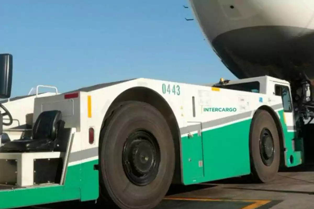 Vehículo remolcador de aviones en pista de aeropuerto junto a la parte frontal de un avión Vehículo remolcador de aviones en pista de aeropuerto junto a la parte frontal de un avión