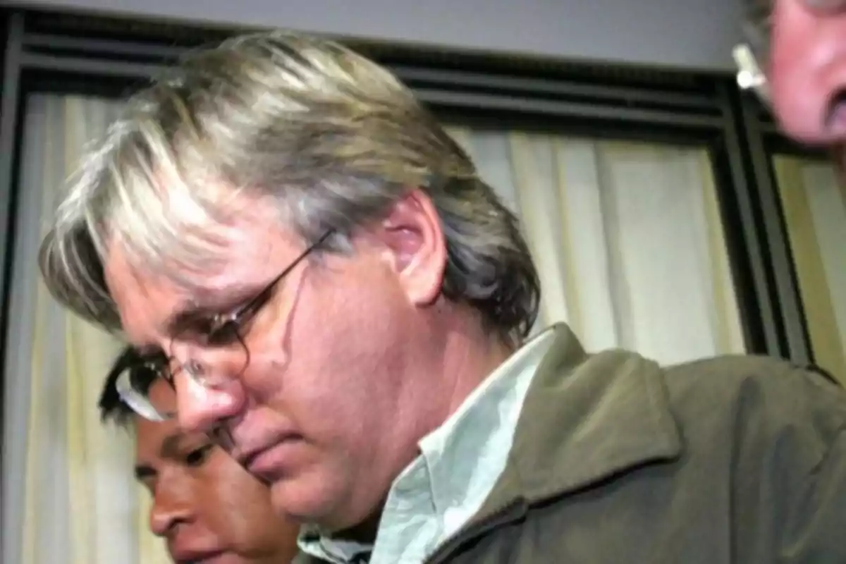 Gray-haired man with glasses looking down with a serious expression in an indoor setting Gray-haired man with glasses looking down with a serious expression in an indoor setting