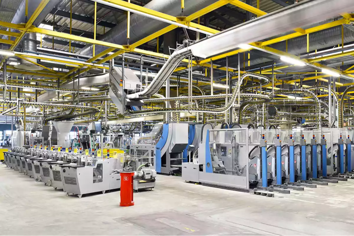Línea de producción automatizada en el interior de una fábrica moderna con maquinaria industrial y estructuras metálicas amarillas