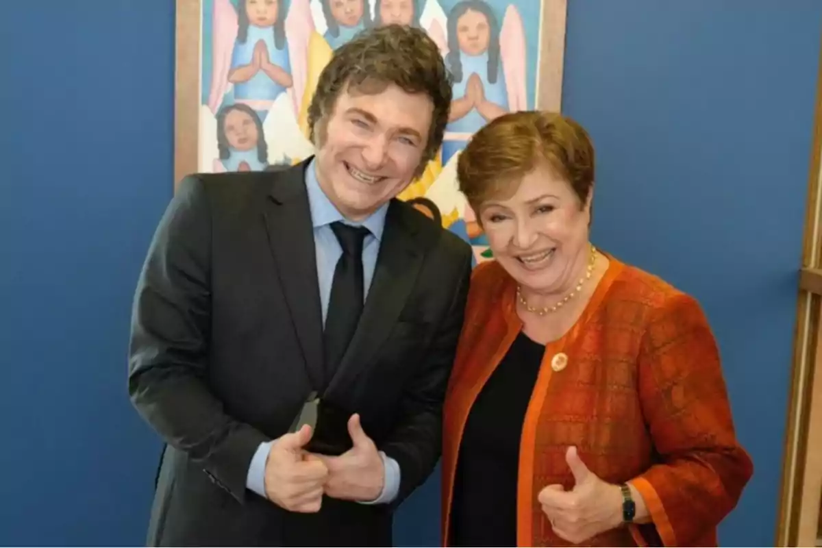 Dos personas sonrientes posan juntas haciendo el gesto de pulgar arriba frente a una pared azul y un cuadro colorido de fondo