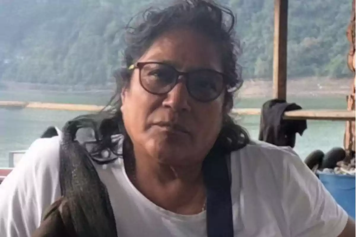 Dark-haired woman with glasses sitting in front of a landscape of lake and mountains Dark-haired woman with glasses sitting in front of a landscape of lake and mountains
