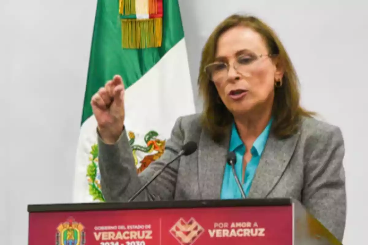 Brown-haired woman with glasses speaking at a podium with the Veracruz coat of arms and a Mexican flag in the background Brown-haired woman with glasses speaking at a podium with the Veracruz coat of arms and a Mexican flag in the background