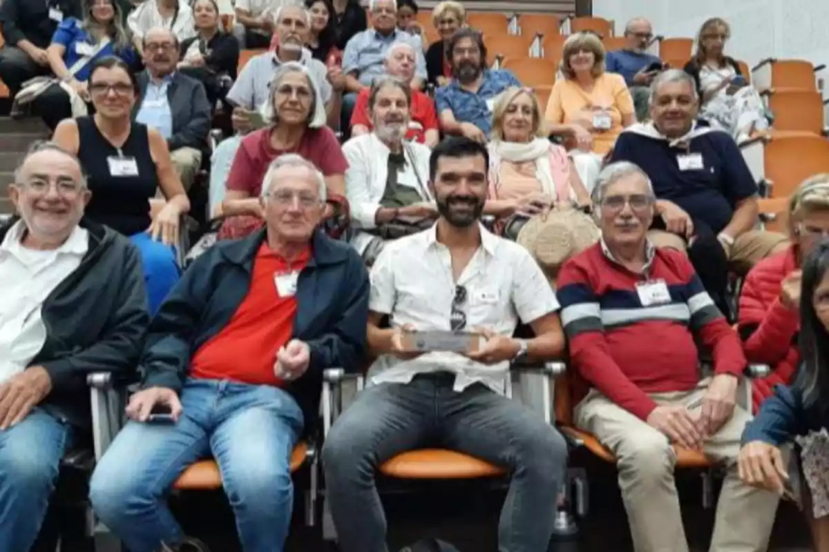Group of people sitting in an auditorium looking at the camera and smiling Group of people sitting in an auditorium looking at the camera and smiling