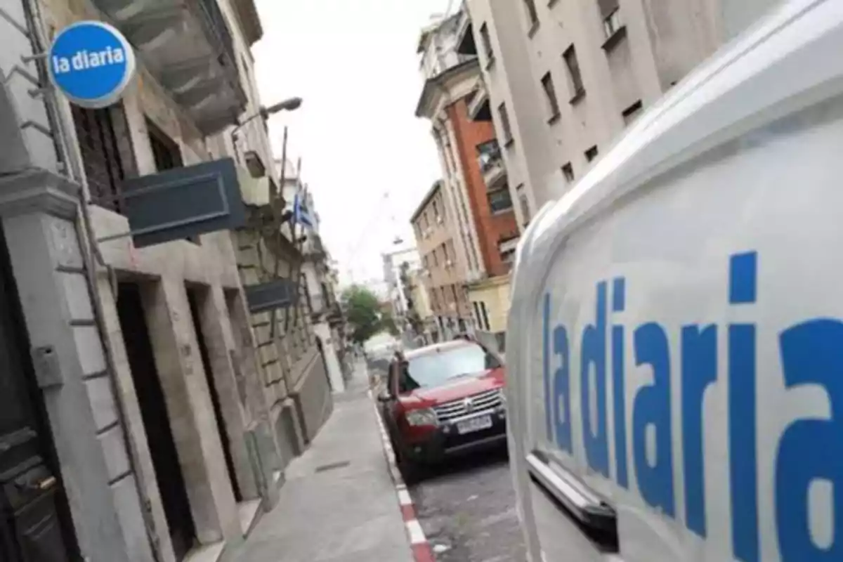 Urban building facade with a blue La Diaria sign and a white van parked with the same logo reflected.