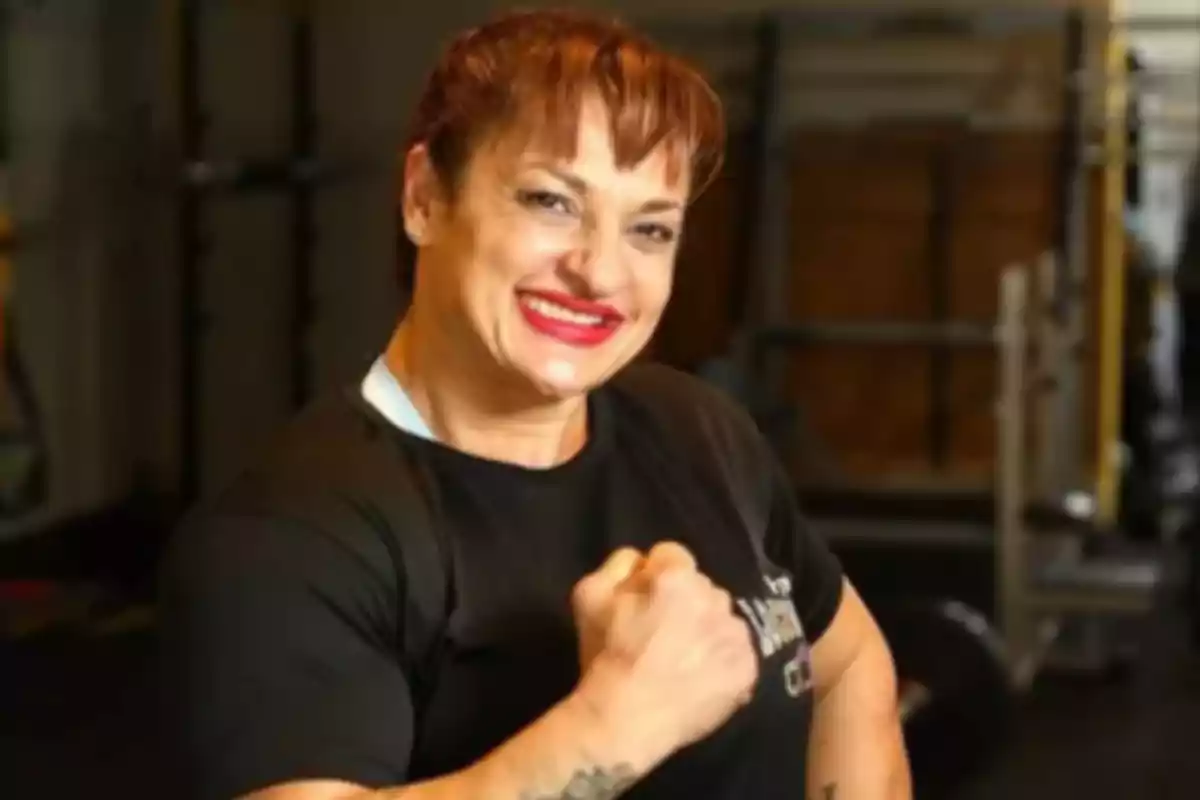 Mujer sonriente con camiseta negra mostrando el puño en un gimnasio Mujer sonriente con camiseta negra mostrando el puño en un gimnasio