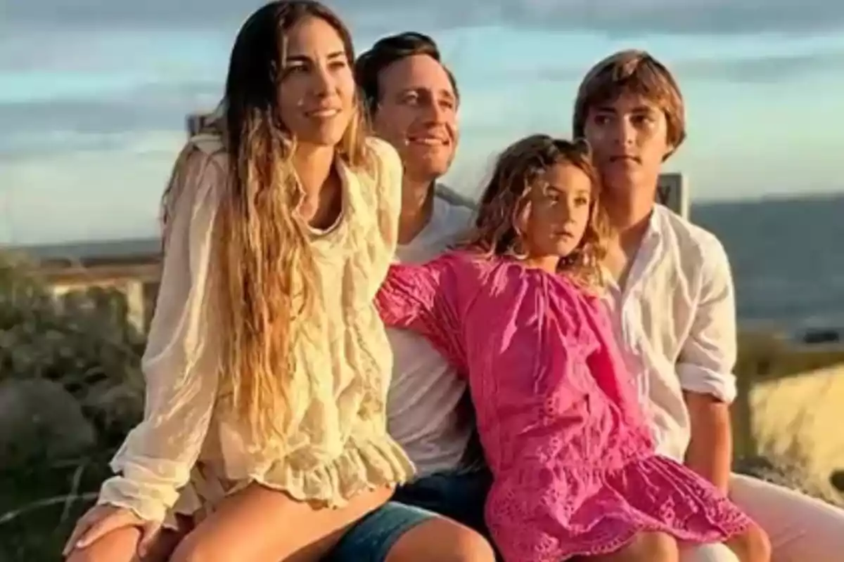 Cuatro personas sentadas al aire libre disfrutando de un atardecer, dos adultos y dos niños, todos con ropa veraniega y expresiones relajadas. Cuatro personas sentadas al aire libre disfrutando de un atardecer, dos adultos y dos niños, todos con ropa veraniega y expresiones relajadas.