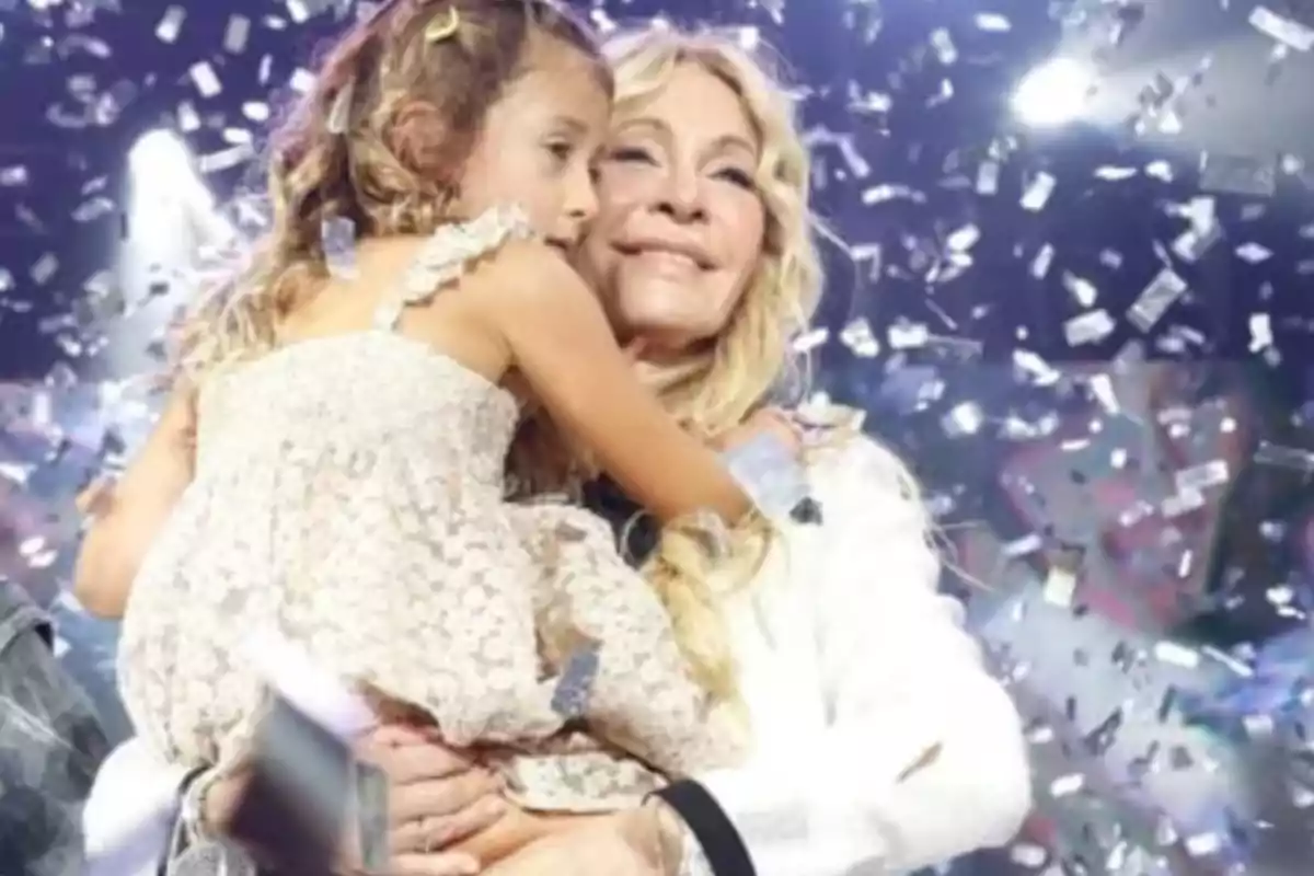 Una mujer sonriente abraza a una niña mientras caen confeti plateado y luces brillan en el fondo