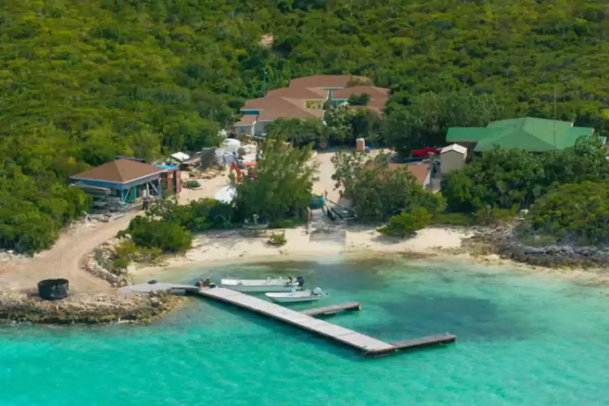 Vista aérea de una pequeña playa con muelle y dos lanchas, rodeada de vegetación y varias casas cerca de la orilla del mar turquesa. Vista aérea de una pequeña playa con muelle y dos lanchas, rodeada de vegetación y varias casas cerca de la orilla del mar turquesa.