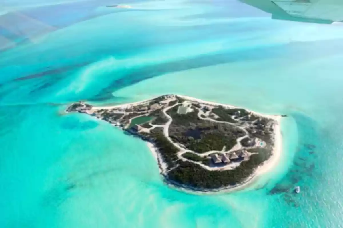 Isla rodeada de aguas turquesa vista desde el aire con algunas construcciones y vegetación Isla rodeada de aguas turquesa vista desde el aire con algunas construcciones y vegetación