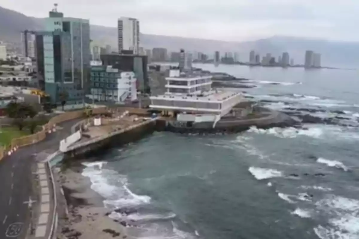 Vista costera de una ciudad con edificios altos junto al mar y un muelle rodeado de olas