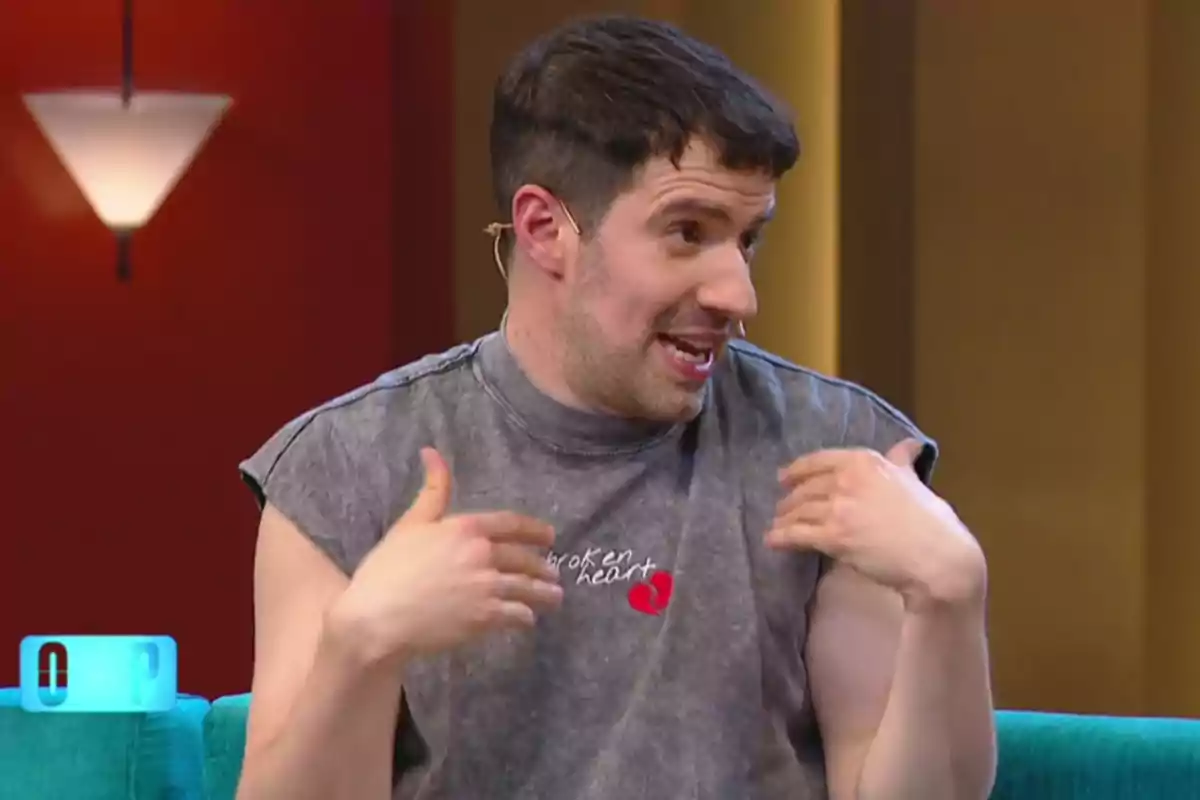Hombre joven con camiseta sin mangas gris hablando y gesticulando en un set de televisión Hombre joven con camiseta sin mangas gris hablando y gesticulando en un set de televisión