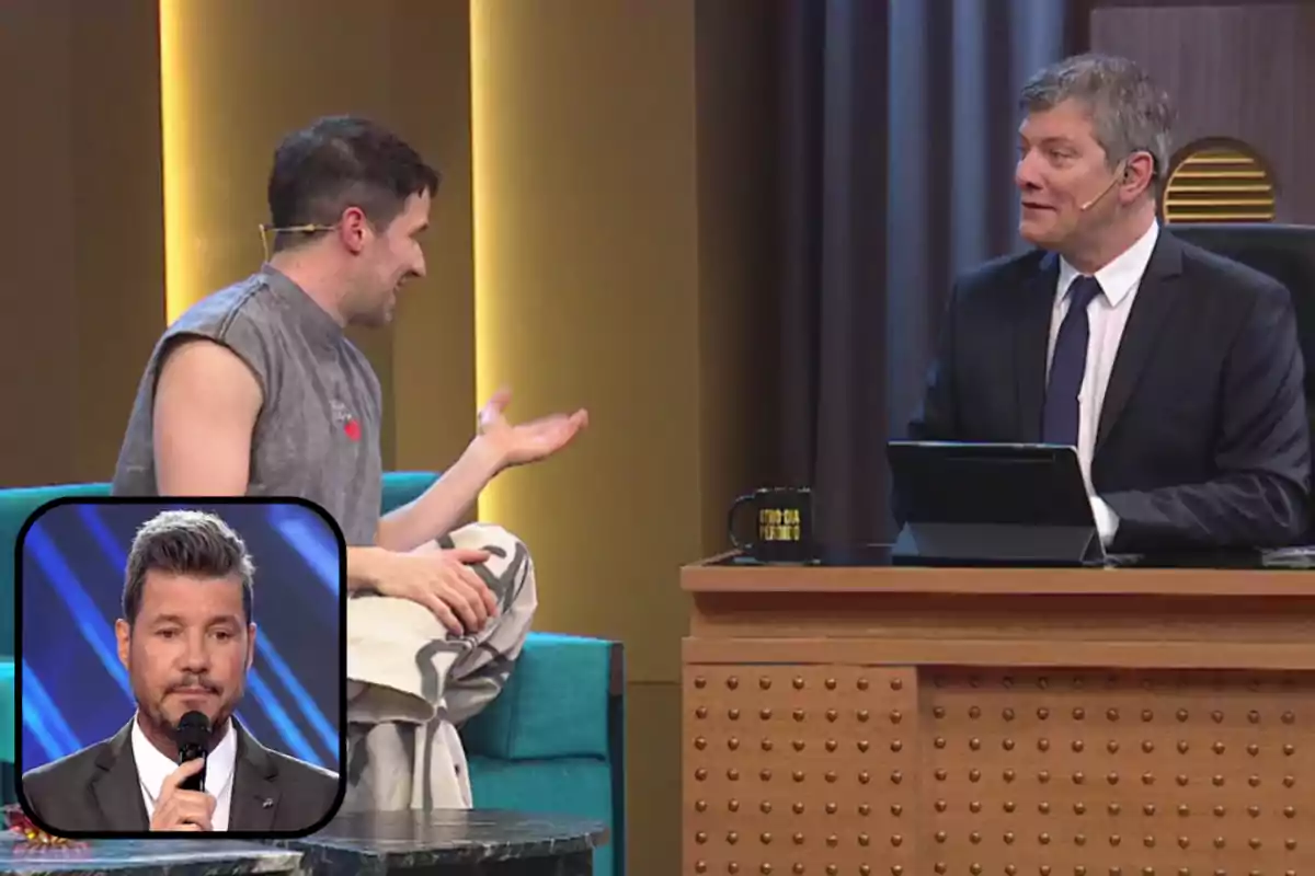 Dos hombres conversan en un set de televisión tipo late night show, uno está sentado en un sillón y el otro detrás de un escritorio, en la esquina inferior izquierda aparece un recuadro con la imagen de otro hombre sosteniendo un micrófono.