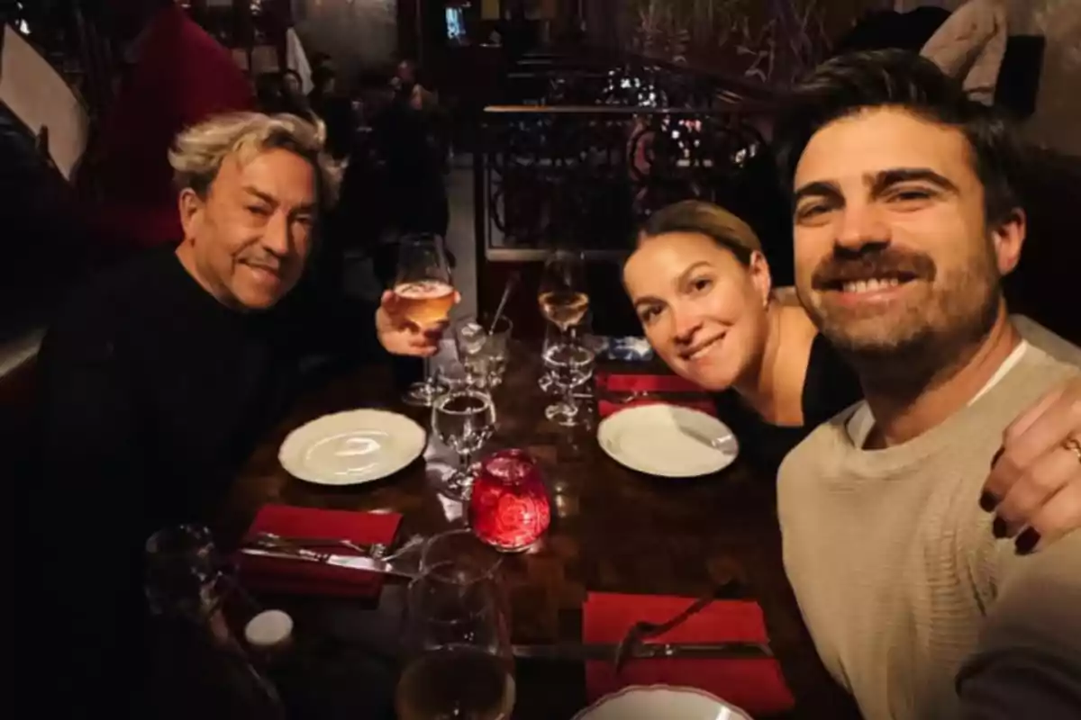 Three people smile as they pose for a photo at a restaurant table with wine glasses and empty plates. Three people smile as they pose for a photo at a restaurant table with wine glasses and empty plates.