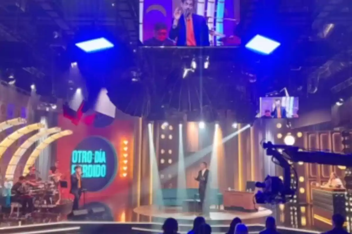 TV set with lights on, musicians to the left, a host in the center, and audience in front TV set with lights on, musicians to the left, a host in the center, and audience in front