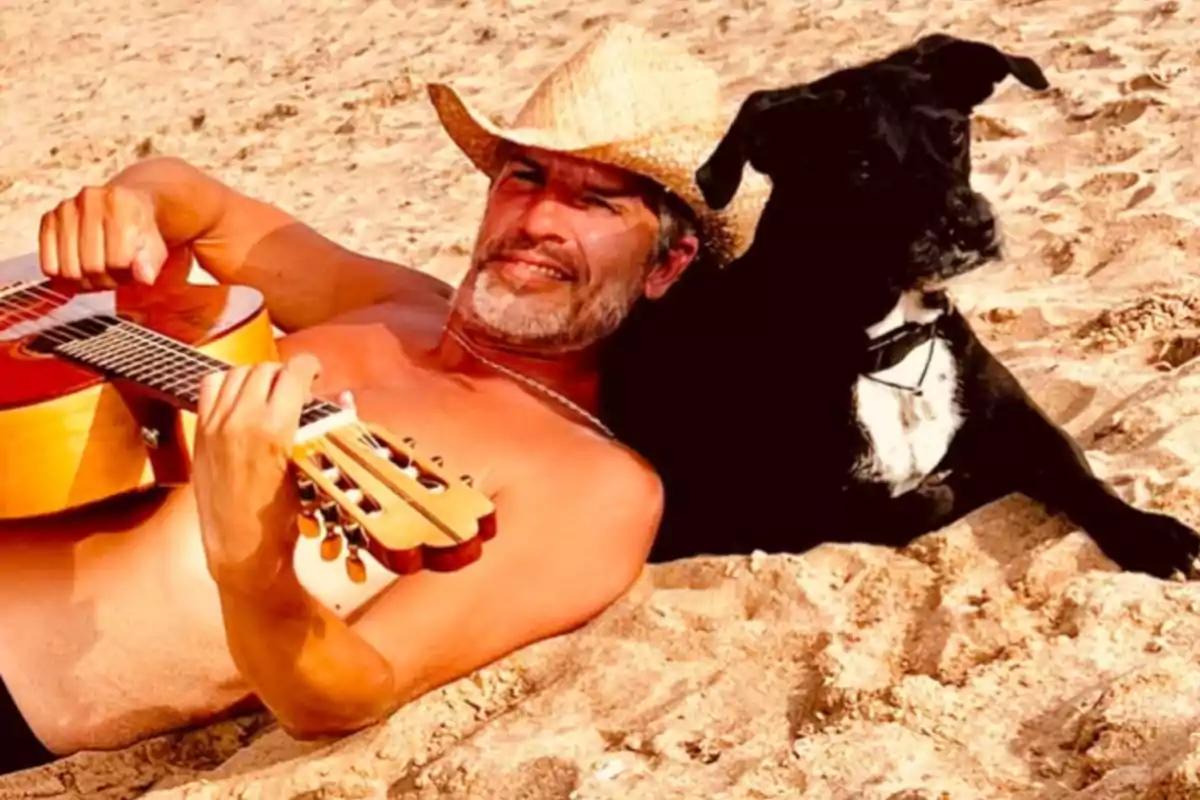 Hombre recostado en la arena tocando una guitarra junto a un perro negro en la playa