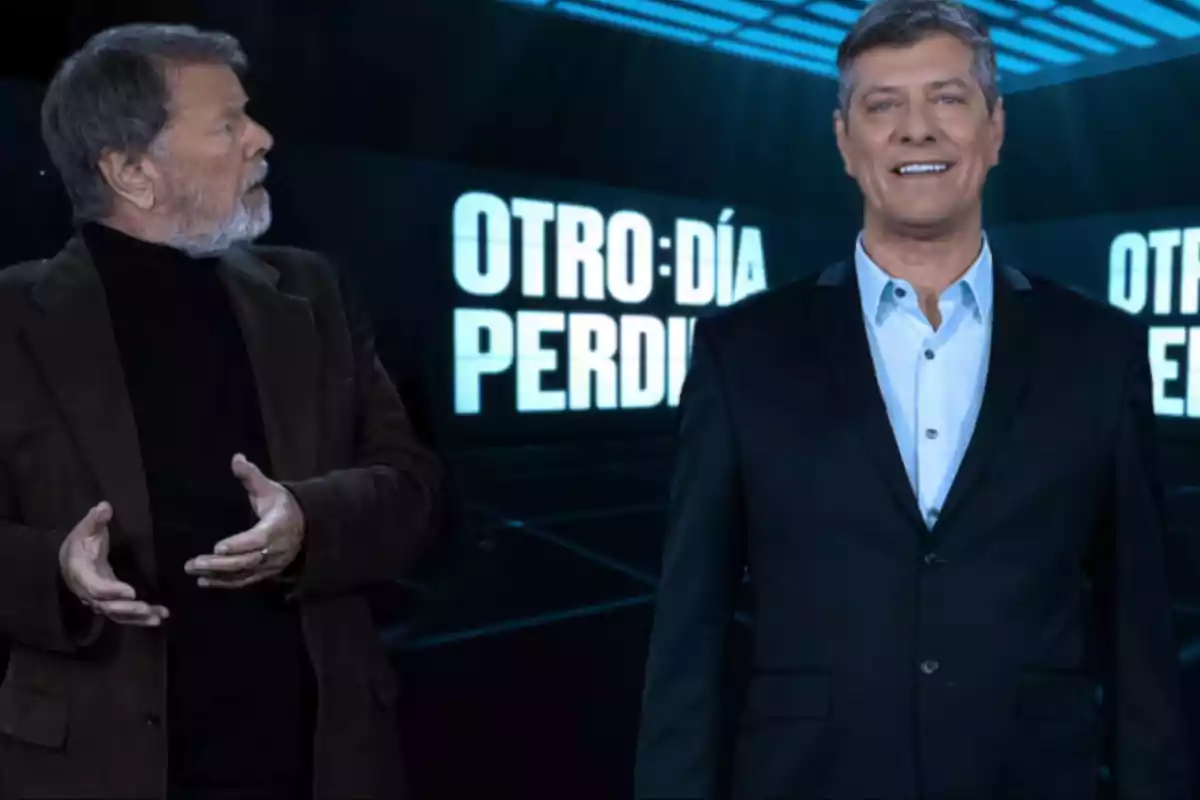 Two men on a television set with background screens displaying the text Two men on a television set with background screens displaying the text