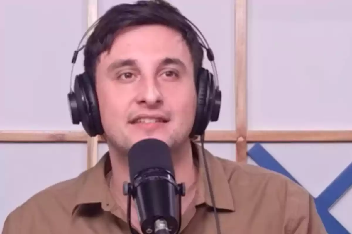 Hombre con audífonos y camisa marrón hablando frente a un micrófono en un estudio de grabación