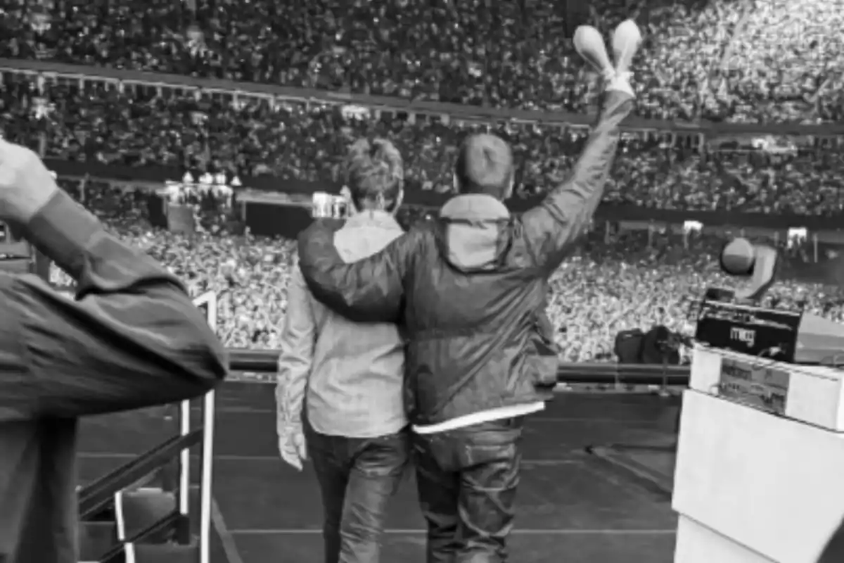 Dos personas de espaldas abrazadas en el escenario de un concierto frente a una multitud