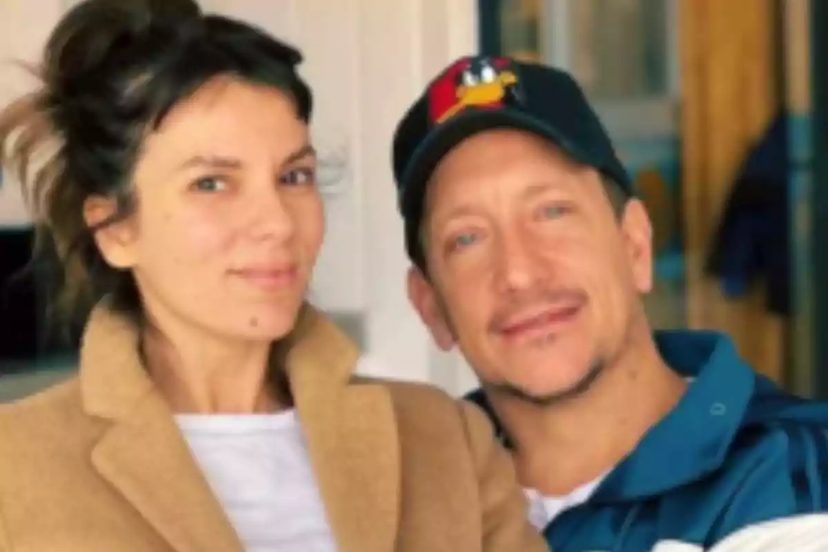 Una mujer con abrigo beige y un hombre con gorra negra posan juntos y sonríen en un ambiente interior iluminado Una mujer con abrigo beige y un hombre con gorra negra posan juntos y sonríen en un ambiente interior iluminado