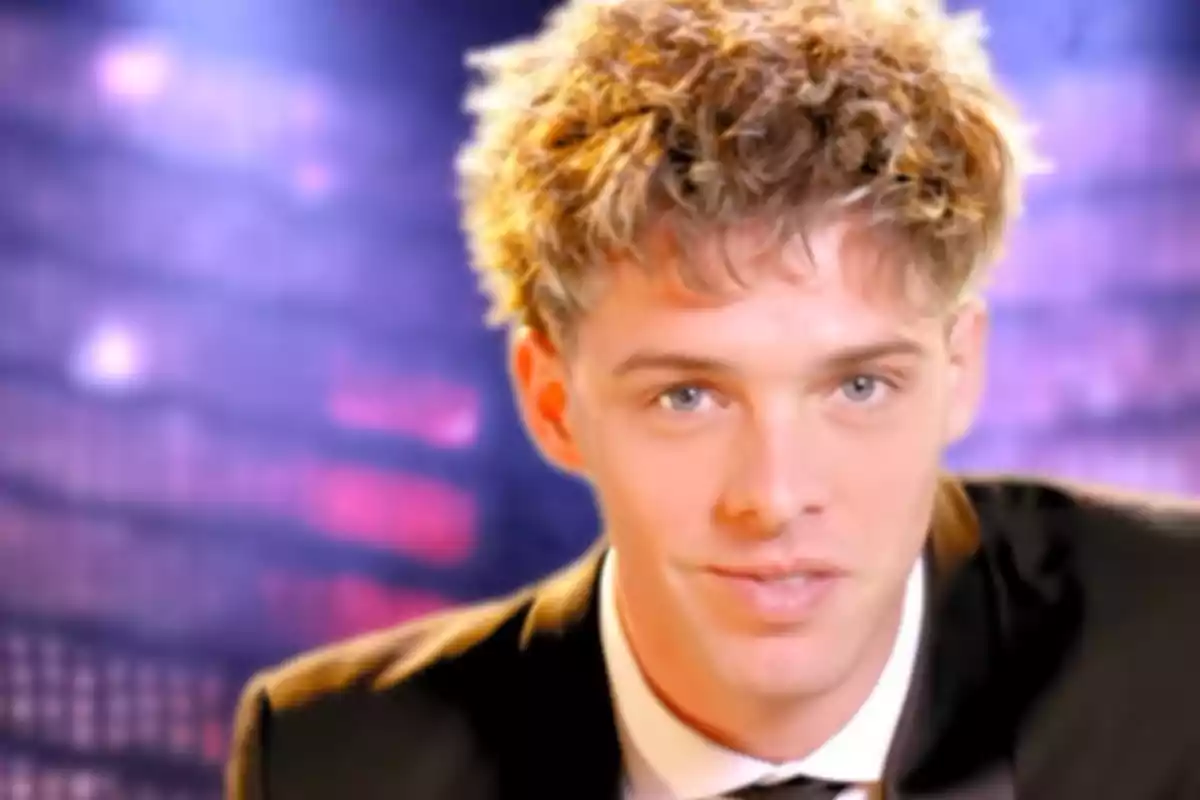 Young man with curly blond hair in a dark suit and a blurred background of purple lights