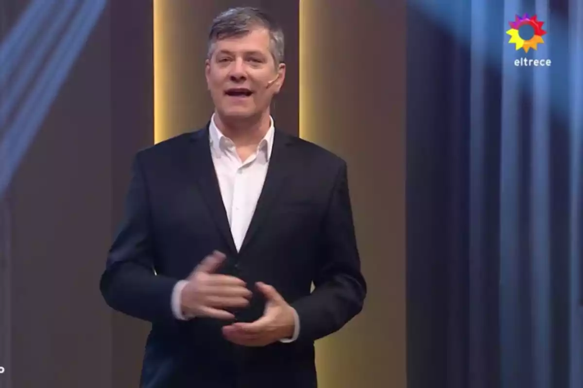 Gray-haired man in a dark suit and white jersey speaking in a television studio with the eltrece logo in the top right corner Gray-haired man in a dark suit and white jersey speaking in a television studio with the eltrece logo in the top right corner