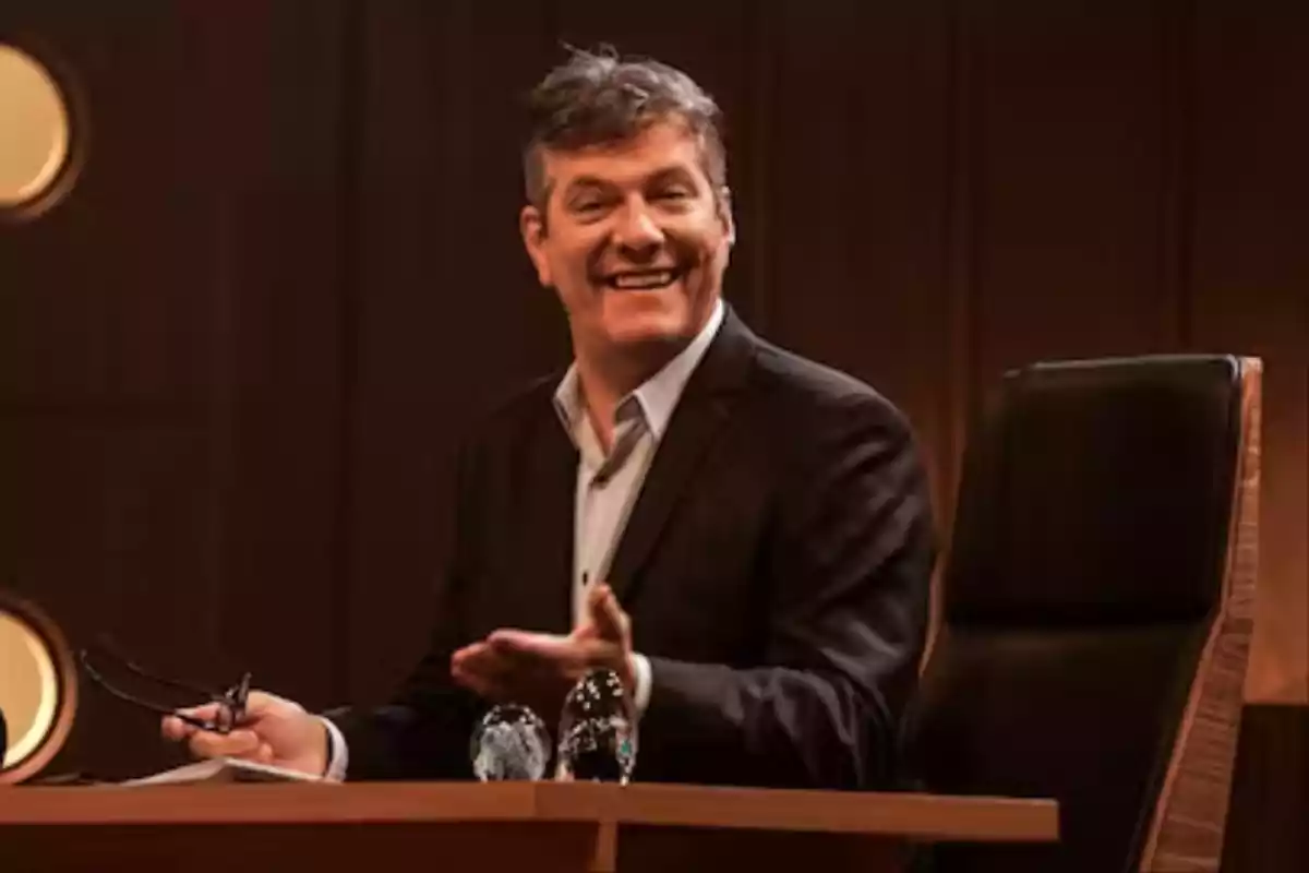Man in a dark suit smiling while sitting in a chair behind a desk in an elegant setting Man in a dark suit smiling while sitting in a chair behind a desk in an elegant setting