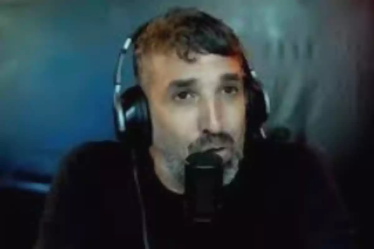 Hombre con audífonos y micrófono hablando frente a una pared azul