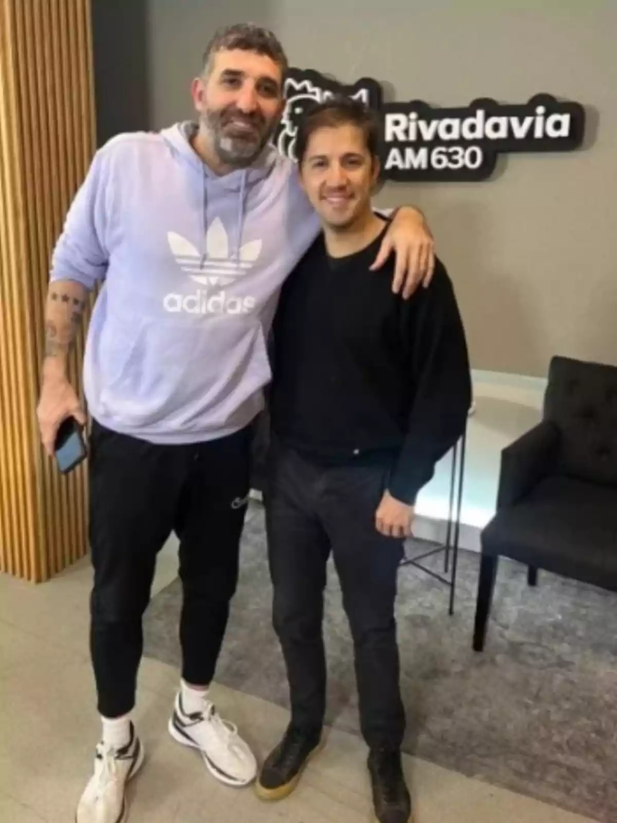 Dos hombres posan juntos sonriendo en una oficina de radio con un cartel de Rivadavia AM 630 al fondo Dos hombres posan juntos sonriendo en una oficina de radio con un cartel de Rivadavia AM 630 al fondo