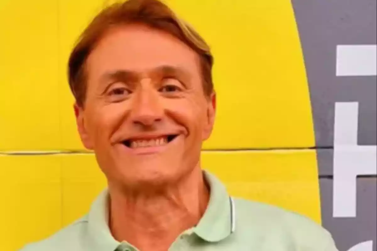 Hombre sonriente con camisa verde claro frente a una pared amarilla y gris