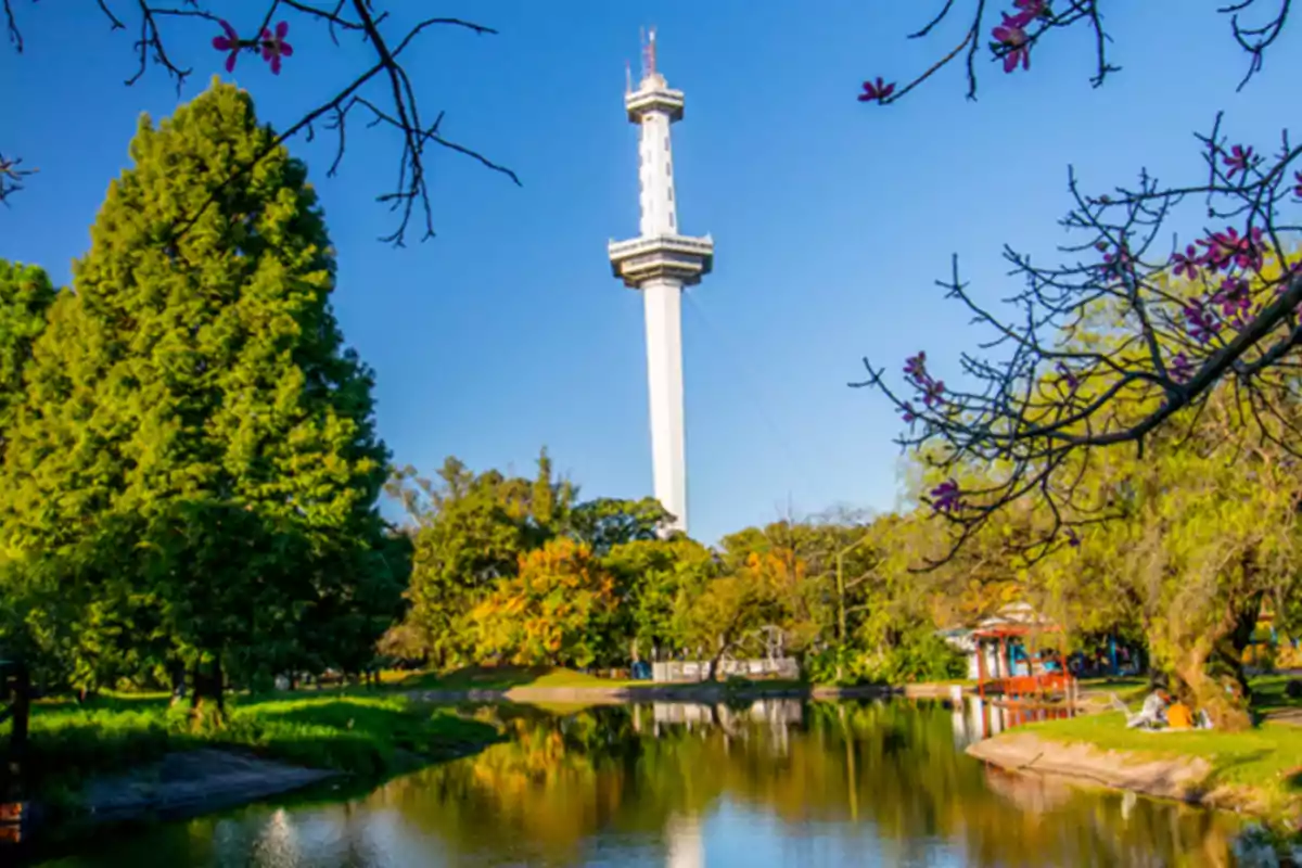 Torre alta blanca rodeada de árboles y un lago en un parque bajo un cielo despejado Torre alta blanca rodeada de árboles y un lago en un parque bajo un cielo despejado