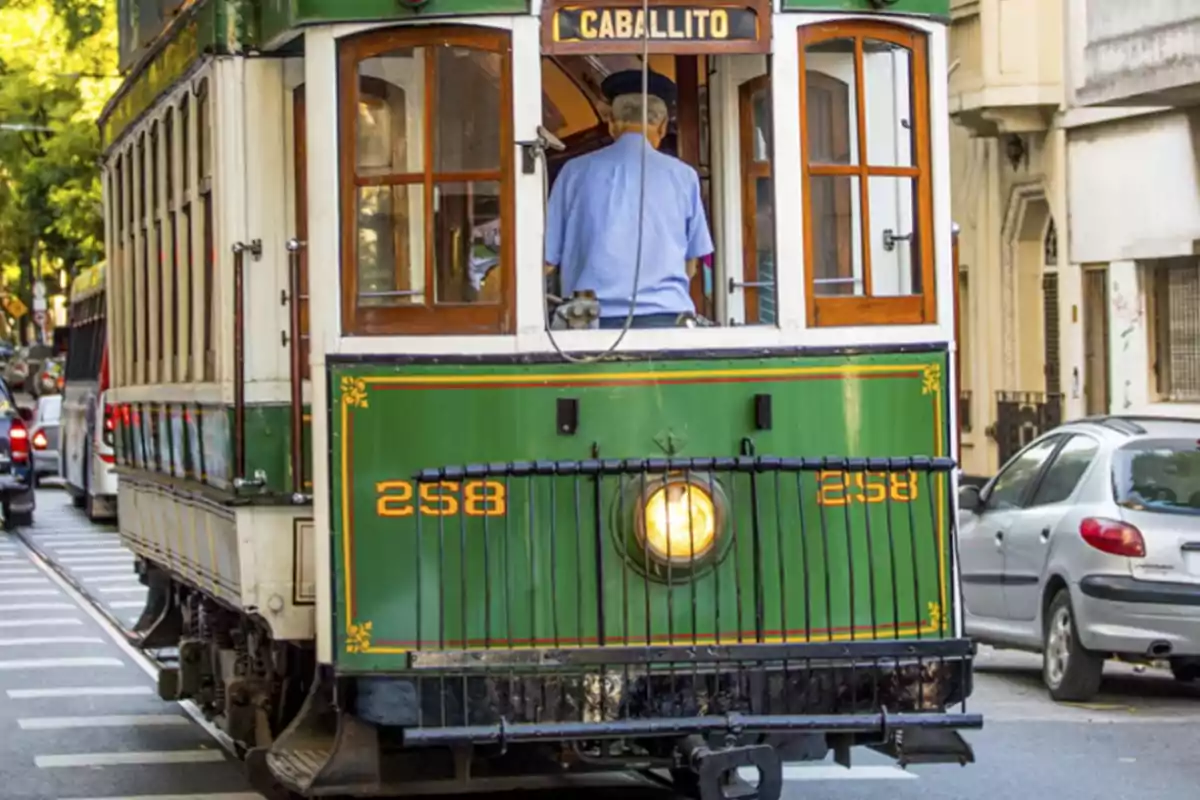 Tranvía antiguo de color verde circulando por una calle urbana con autos estacionados y un conductor de uniforme azul Tranvía antiguo de color verde circulando por una calle urbana con autos estacionados y un conductor de uniforme azul