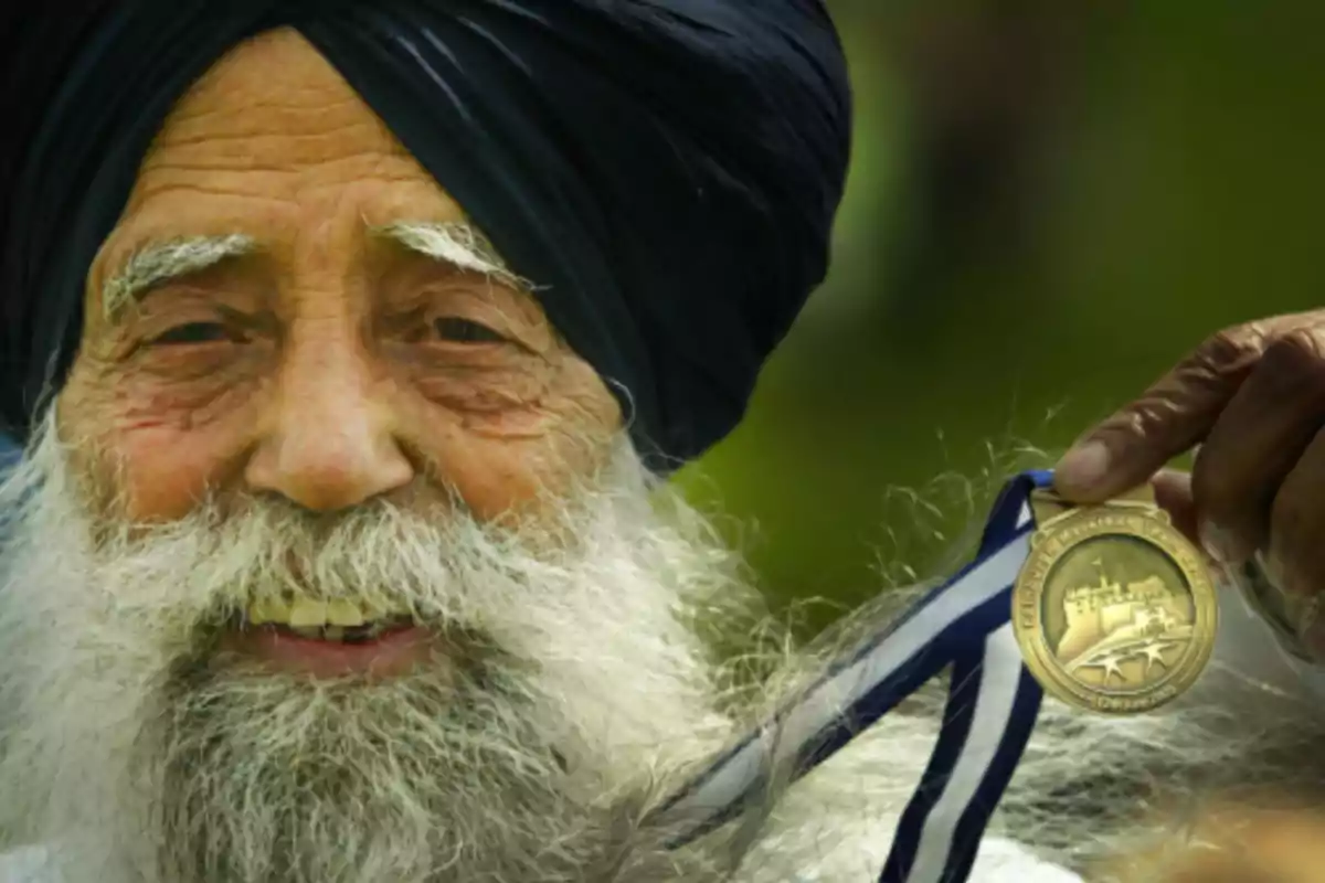 Older man with a white beard and dark turban smiles while holding a gold medal Older man with a white beard and dark turban smiles while holding a gold medal