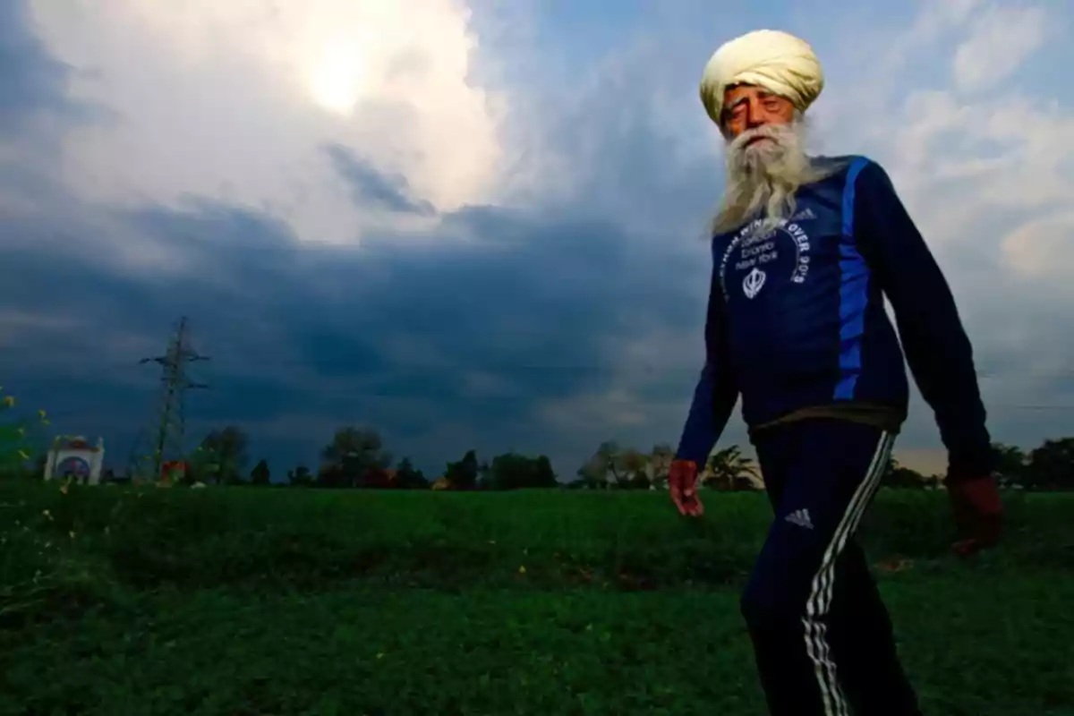 Older man with a beard and turban walking through a green field under a cloudy sky Older man with a beard and turban walking through a green field under a cloudy sky