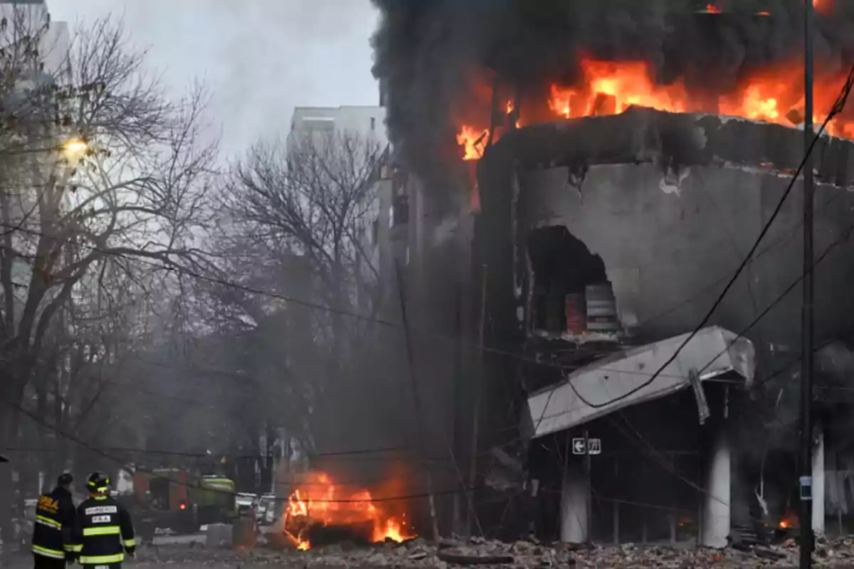 Building on fire with black smoke and debris on the street as firefighters watch the scene Building on fire with black smoke and debris on the street as firefighters watch the scene