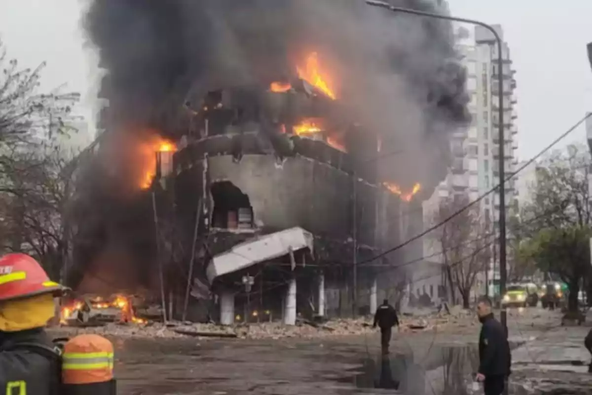 Building on fire with black smoke and firefighters working at the scene while debris covers the street Building on fire with black smoke and firefighters working at the scene while debris covers the street