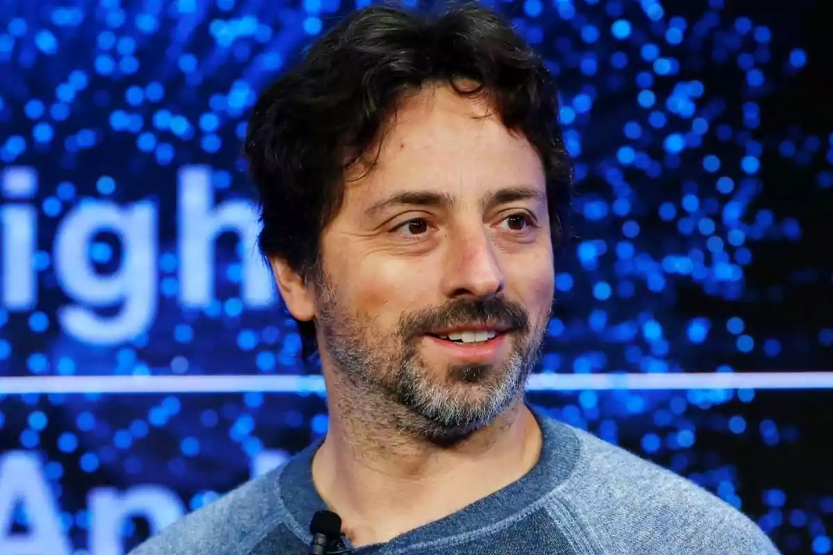 Hombre de cabello oscuro y barba corta sonriendo con un fondo azul lleno de luces desenfocadas Hombre de cabello oscuro y barba corta sonriendo con un fondo azul lleno de luces desenfocadas