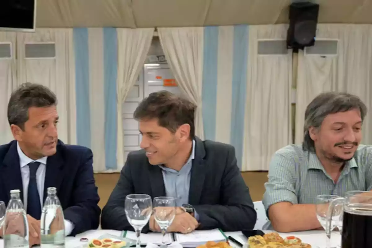 Three men sitting at a table with food and drinks, talking and smiling in a formal setting with white and light blue curtains in the background. Three men sitting at a table with food and drinks, talking and smiling in a formal setting with white and light blue curtains in the background.