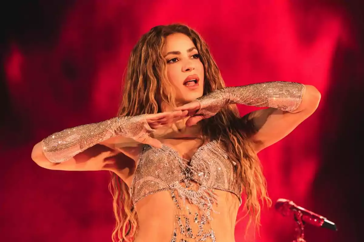 Mujer con cabello largo y ondulado usando un top brillante y guantes plateados mientras baila sobre un fondo rojo