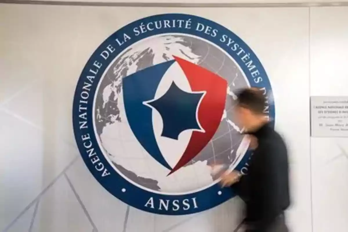 Person walking in front of the logo of the French National Agency for the Security of Information Systems on a white wall Person walking in front of the logo of the French National Agency for the Security of Information Systems on a white wall