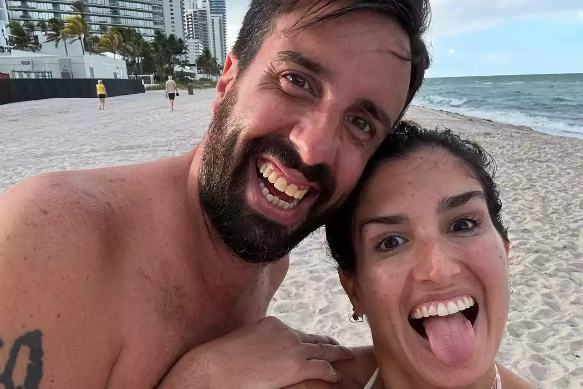 Smiling couple taking a selfie on the beach with buildings and palm trees in the background