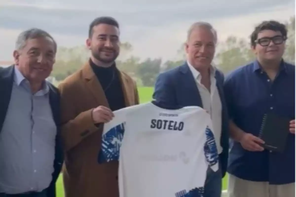 Cuatro hombres posan juntos mientras uno de ellos sostiene una camiseta de fútbol blanca con el nombre Sotelo en la parte trasera.