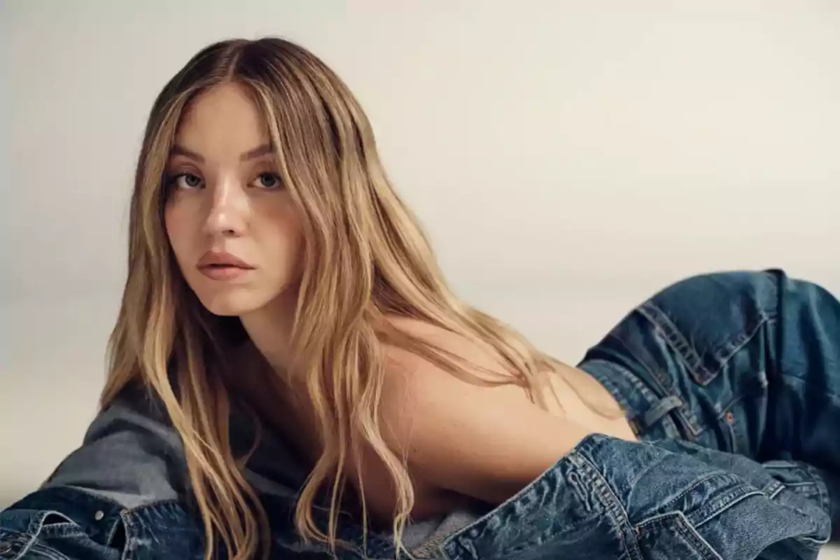 Young woman with long, loose blonde hair lying on a light surface wearing denim clothing