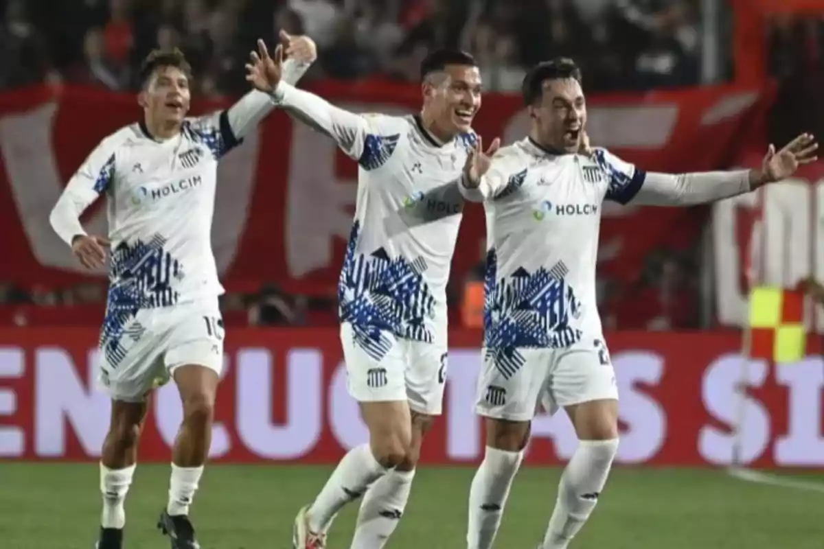 Tres futbolistas con uniforme blanco celebran un gol en un estadio lleno de aficionados Tres futbolistas con uniforme blanco celebran un gol en un estadio lleno de aficionados