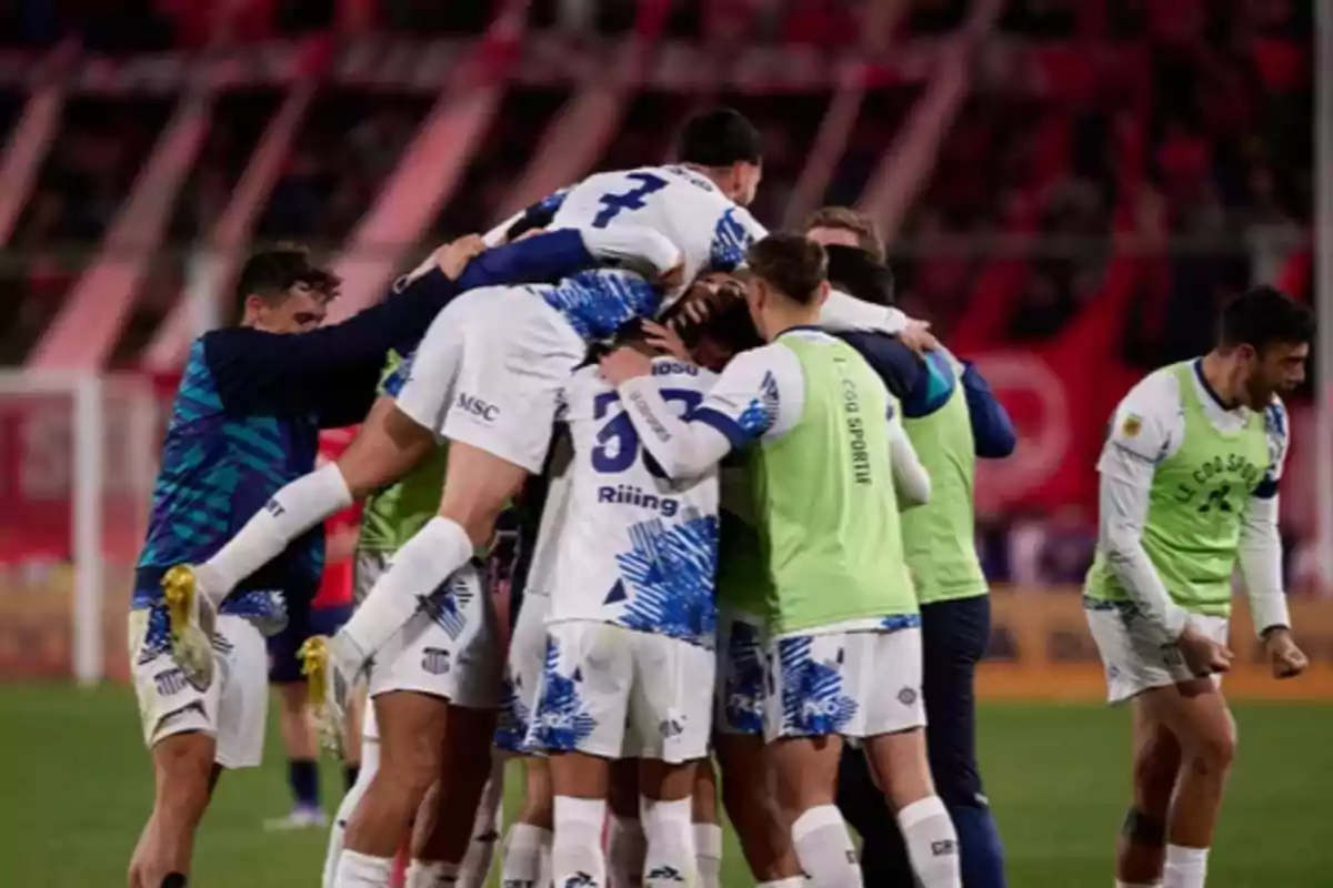 Jugadores de fútbol celebran un gol abrazándose en grupo en el campo durante un partido