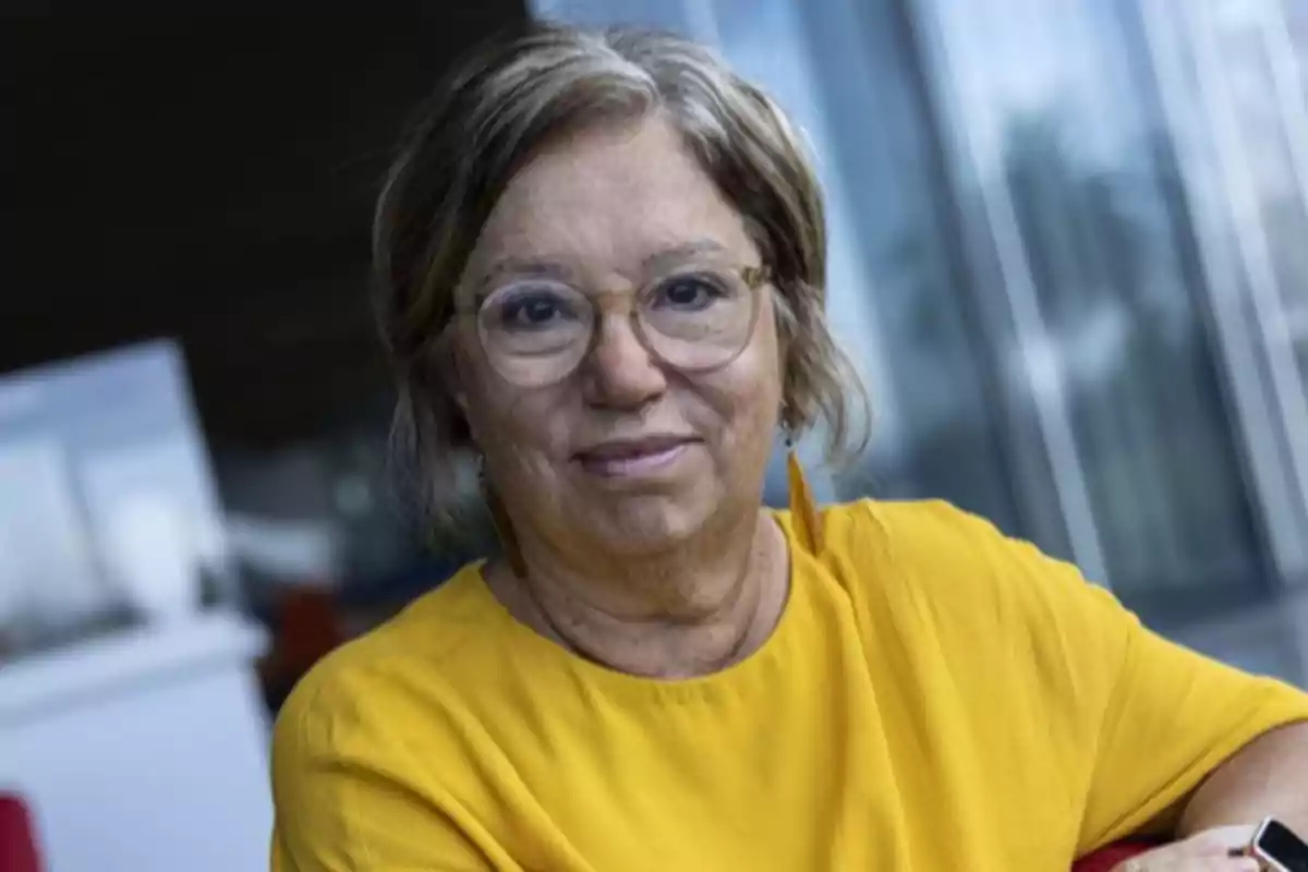 Short-haired, gray-haired woman with glasses and a yellow blouse sitting in a bright indoor setting Short-haired, gray-haired woman with glasses and a yellow blouse sitting in a bright indoor setting