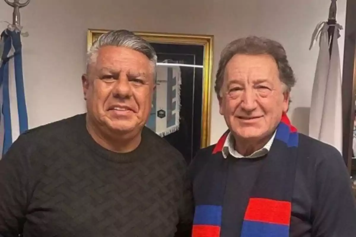 Dos hombres posan juntos y sonríen en una oficina decorada con banderas y un cuadro en la pared Dos hombres posan juntos y sonríen en una oficina decorada con banderas y un cuadro en la pared