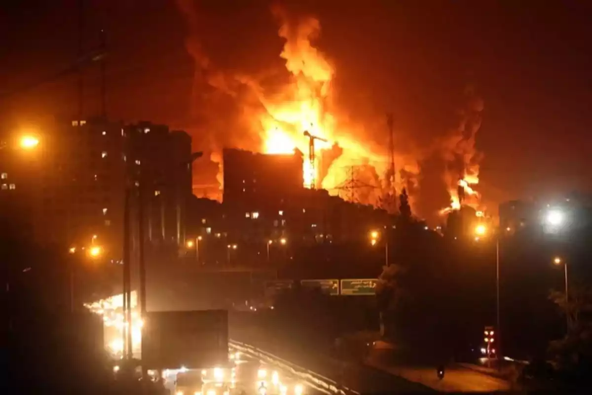 Incendio de gran magnitud en un edificio durante la noche con humo y llamas visibles y una carretera iluminada en primer plano