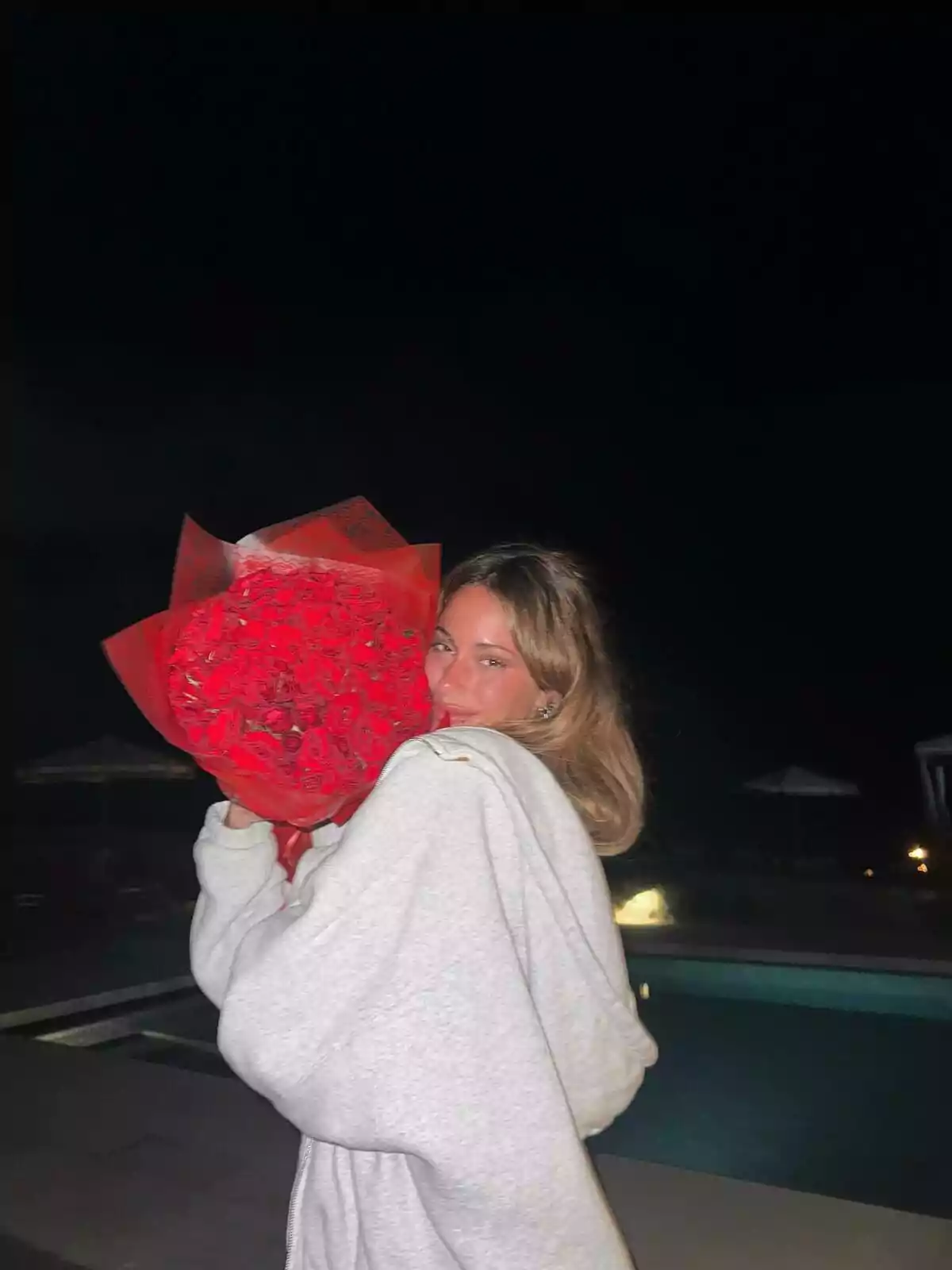 Girl in a gray sweatjersey holding a large bouquet of red roses by a pool at night Girl in a gray sweatjersey holding a large bouquet of red roses by a pool at night