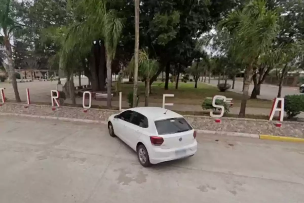 White car parked in front of large letters spelling the name of a city in a park with trees and benches. White car parked in front of large letters spelling the name of a city in a park with trees and benches.