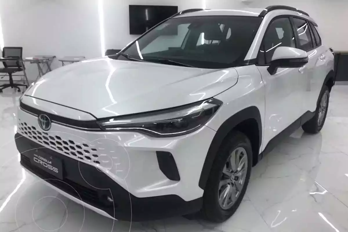 White Toyota Corolla Cross pickup truck parked in a showroom with marble flooring and office furniture in the background White Toyota Corolla Cross pickup truck parked in a showroom with marble flooring and office furniture in the background